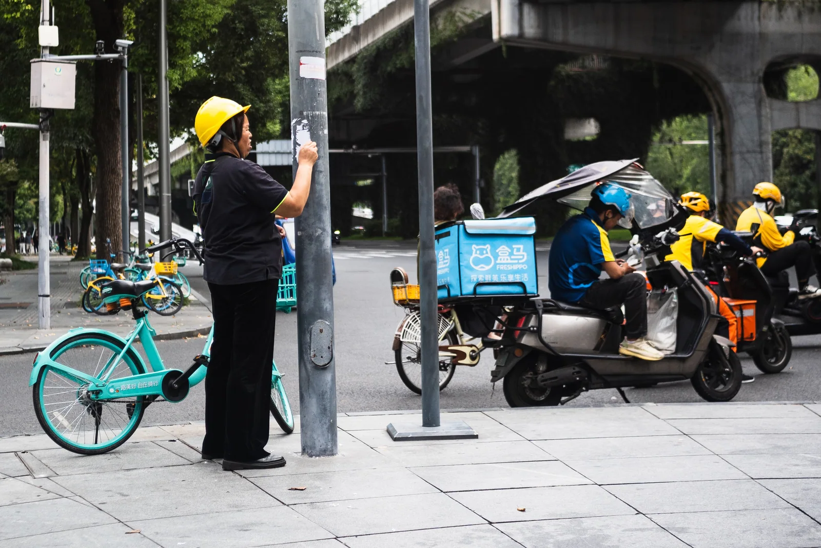 路口站立的黄头盔行人与旁边的自行车、骑手