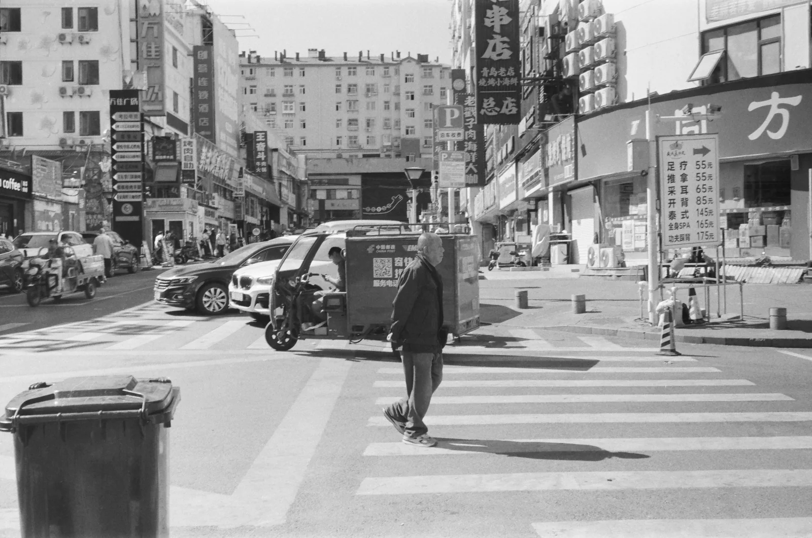 城市街口的斑马线上，一名行人从车辆与店铺间走过