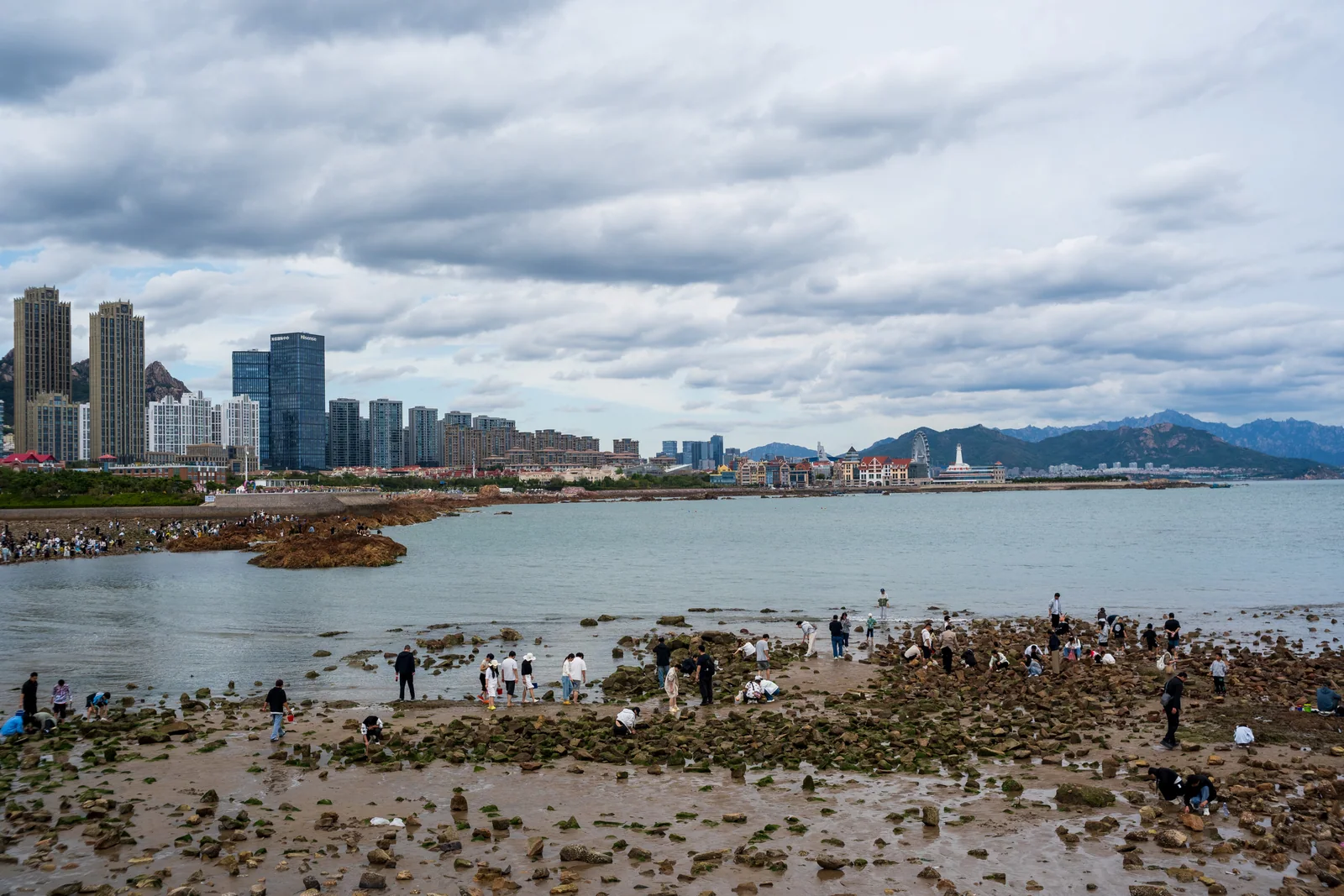 退潮的海湾与城市建筑之间，游客在滩涂上游玩