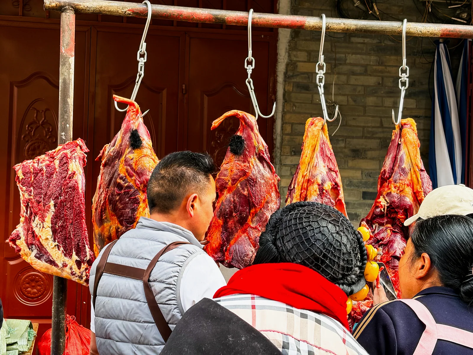 肉铺前悬挂的肉与挑选商品的人